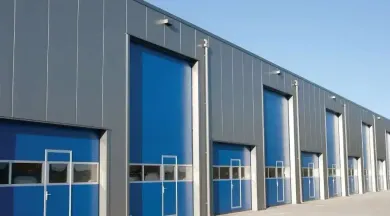 Exterior of a building with multiple blue roll-up doors, silver panels, and a clear sky.