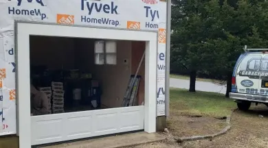 Garage door frame under construction with Tyvek house wrap. White frame, partially open. Van parked to the right.