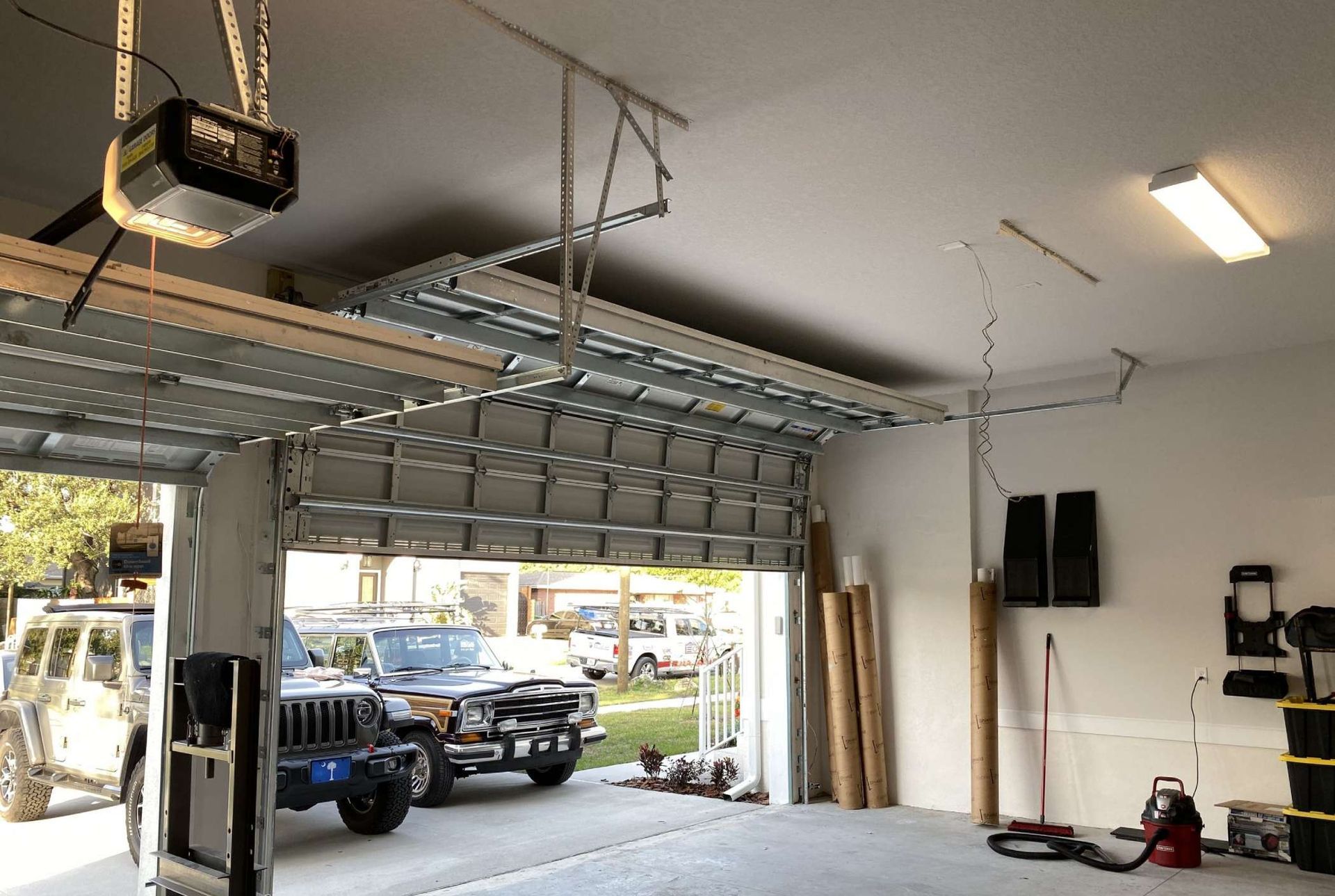 Open garage with vehicles inside; ceiling-mounted garage door opener and lights.