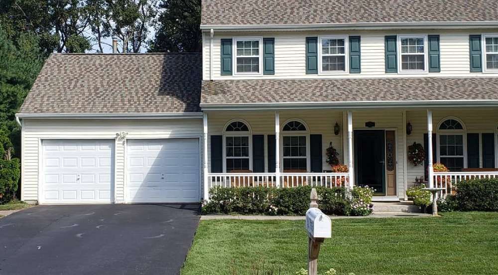 Two-story beige house with two-car garage, porch, green shutters, and a black driveway.
