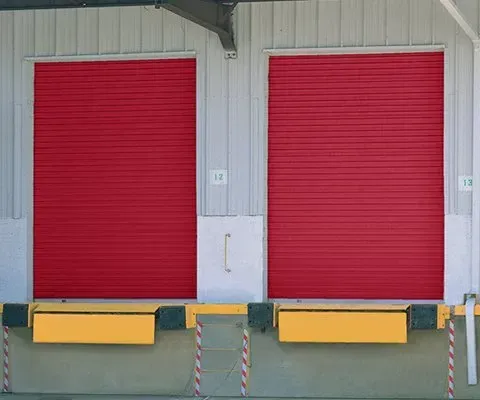 Red roller doors at loading docks, yellow bumpers. Gray and white warehouse exterior.