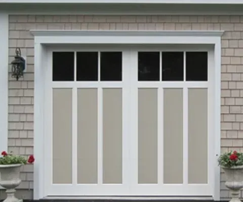 Beige and white garage door with glass panes, set in a light brown shingled wall.
