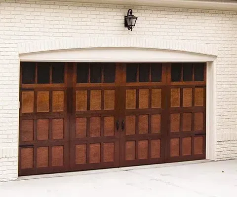 Dark stained wooden garage door on a white brick building with a decorative light fixture.