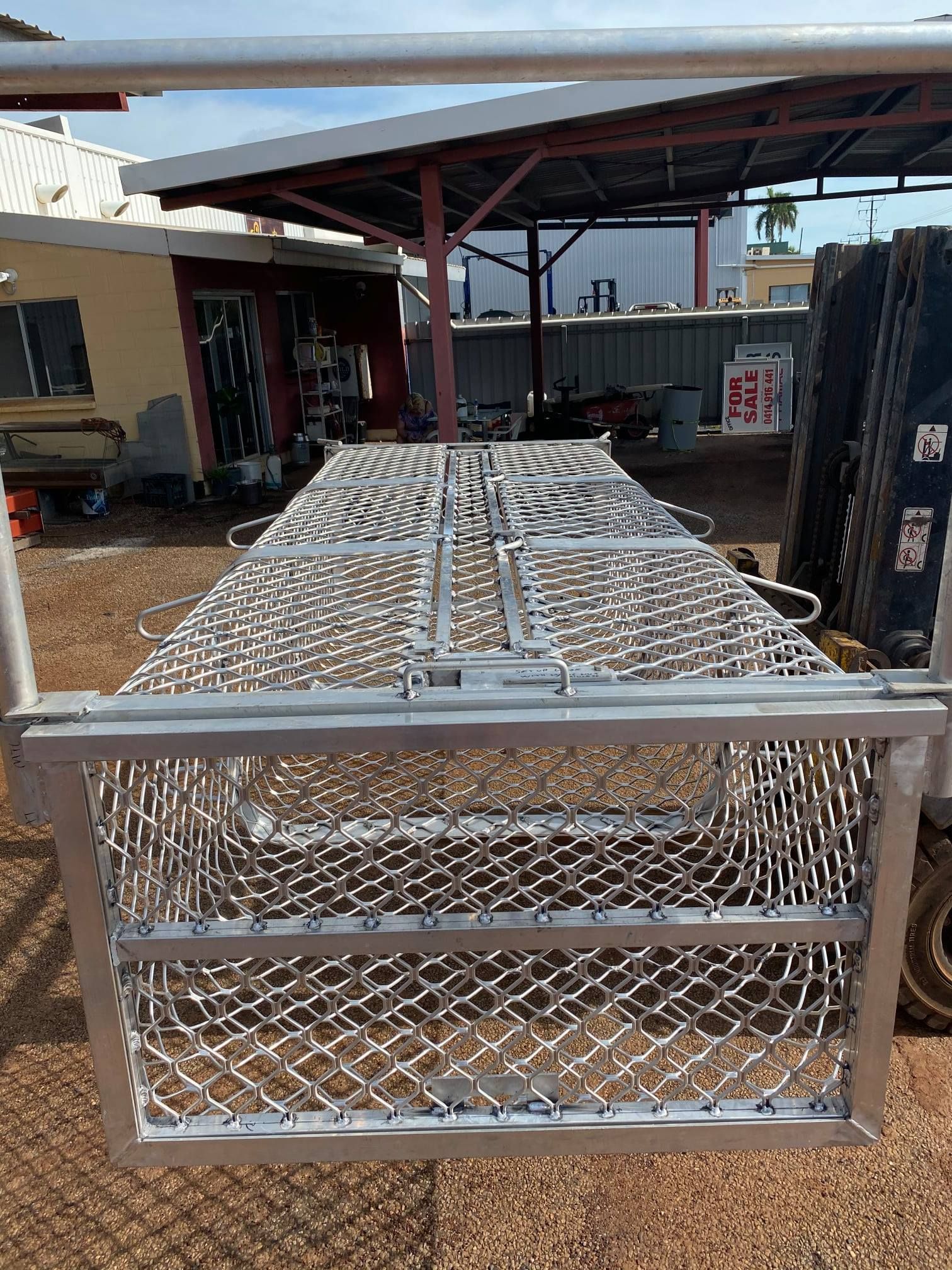 Silver Mesh Livestock Cage Trailer Parked Outdoors Under a Red-roofed Structure — Greville Fabrication in Girraween, NSW