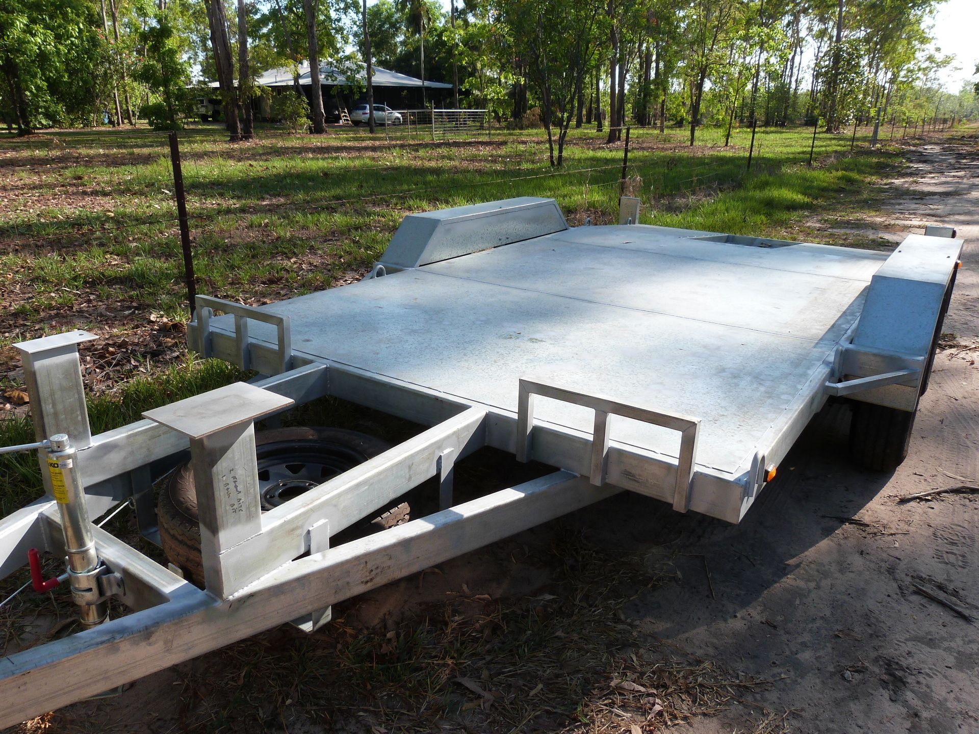 Gray Flatbed Trailer on a Dirt Road, With Side Rails and a Spare Tire Visible — Greville Fabrication in Girraween, NSW