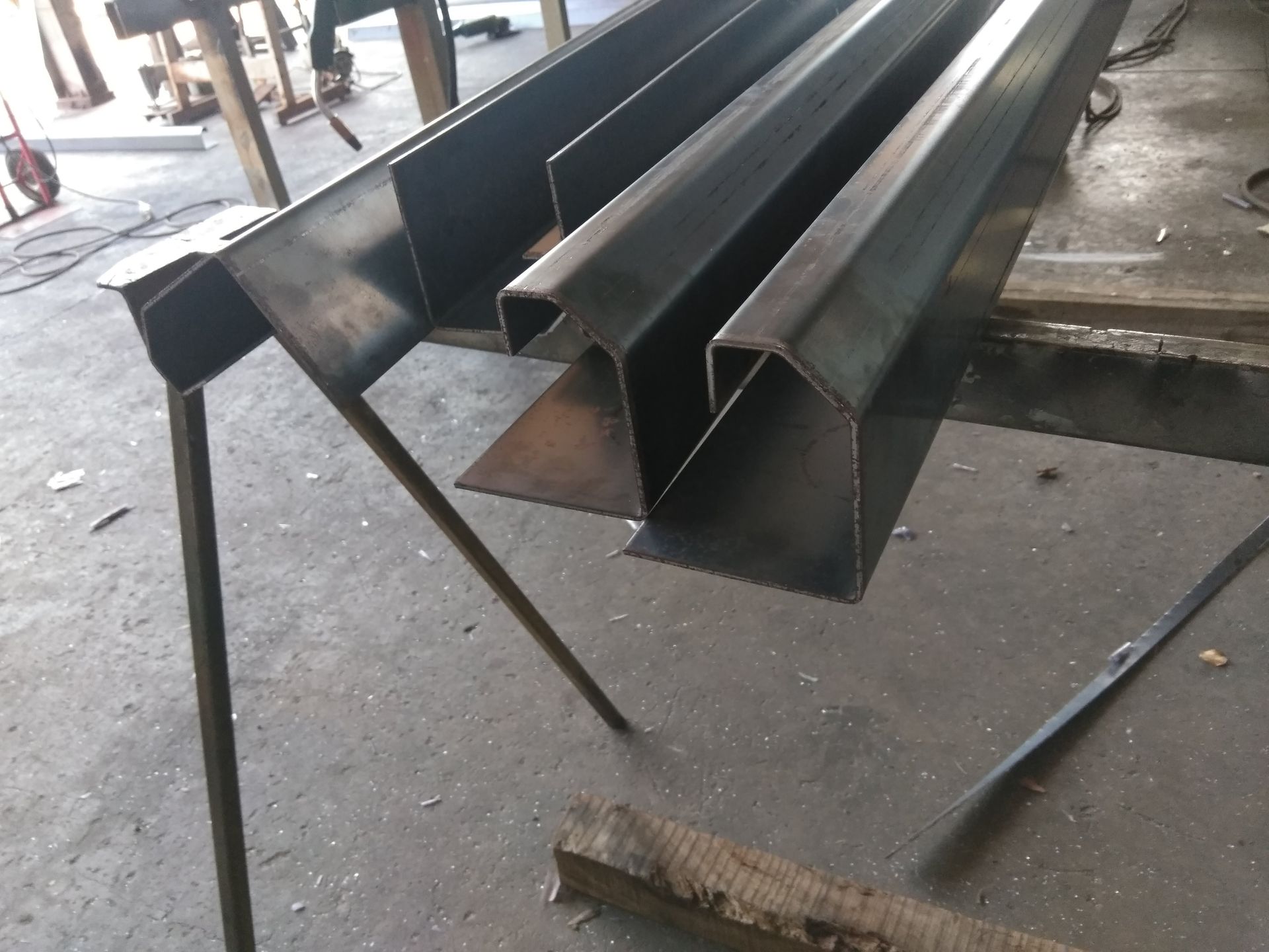 Stacks of Dark Metal Beams and Channels on a Floor, With a Long Rod Beside Them — Greville Fabrication in Girraween, NSW