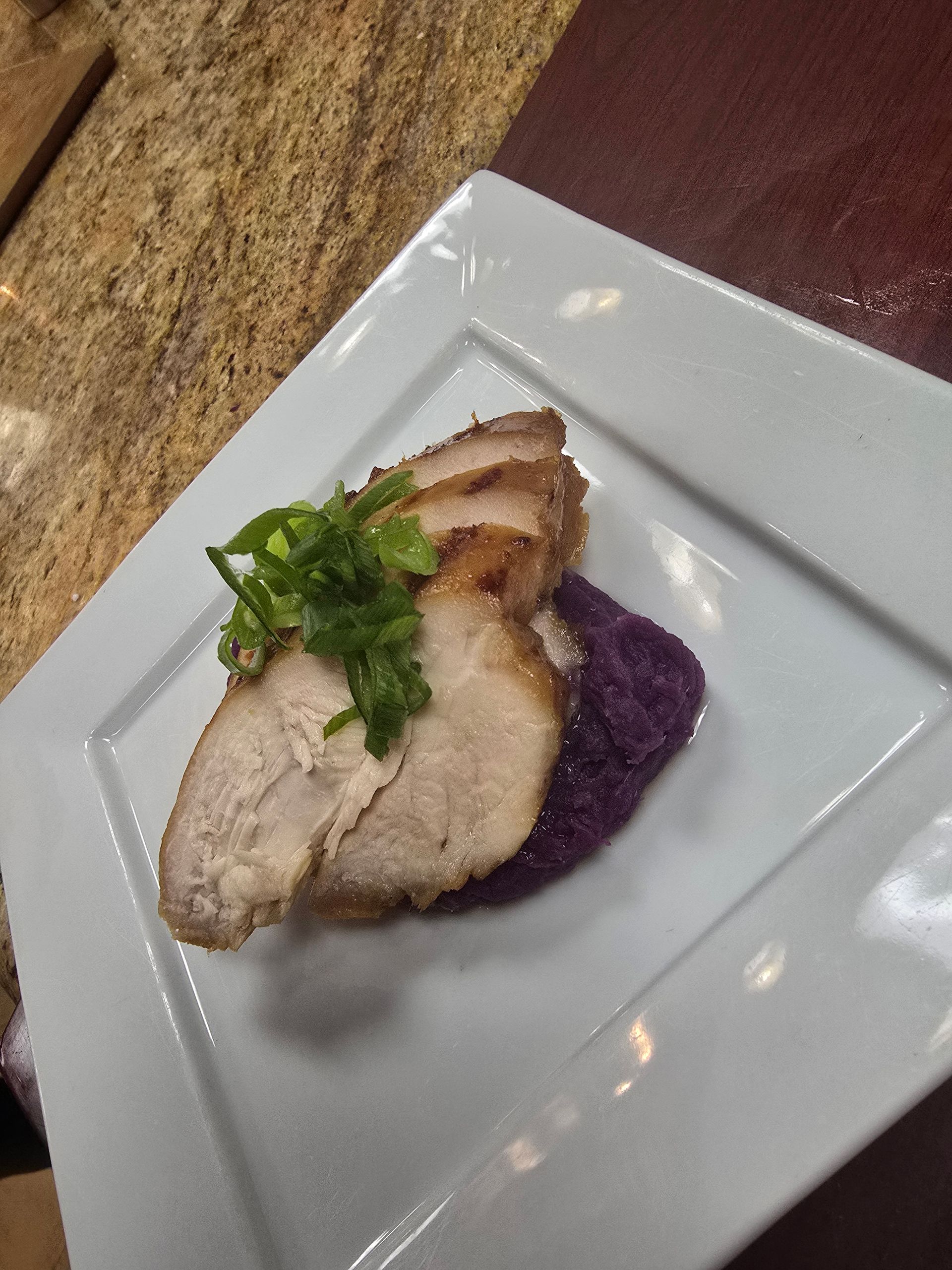 Sliced roasted pork over purple mashed potatoes, garnished with green herbs, on a white plate.