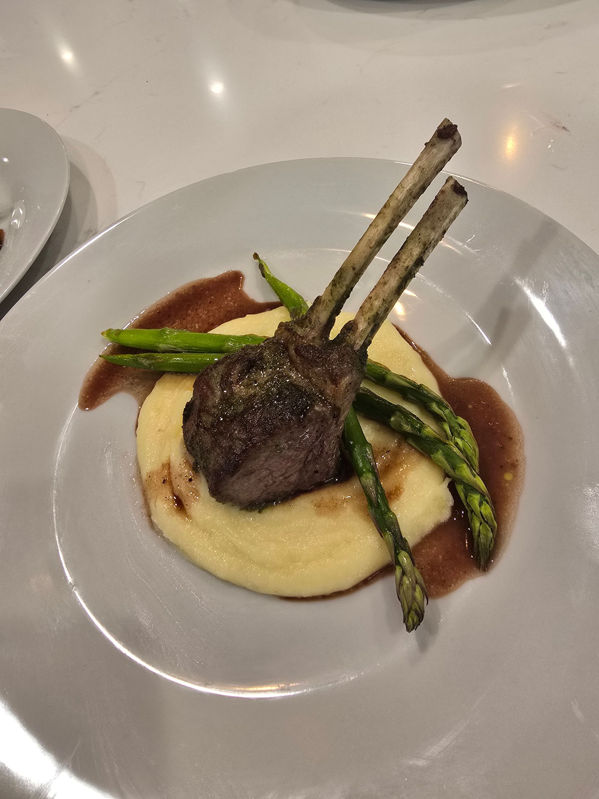 Rack of lamb, asparagus, and polenta on a white plate, with a red sauce.
