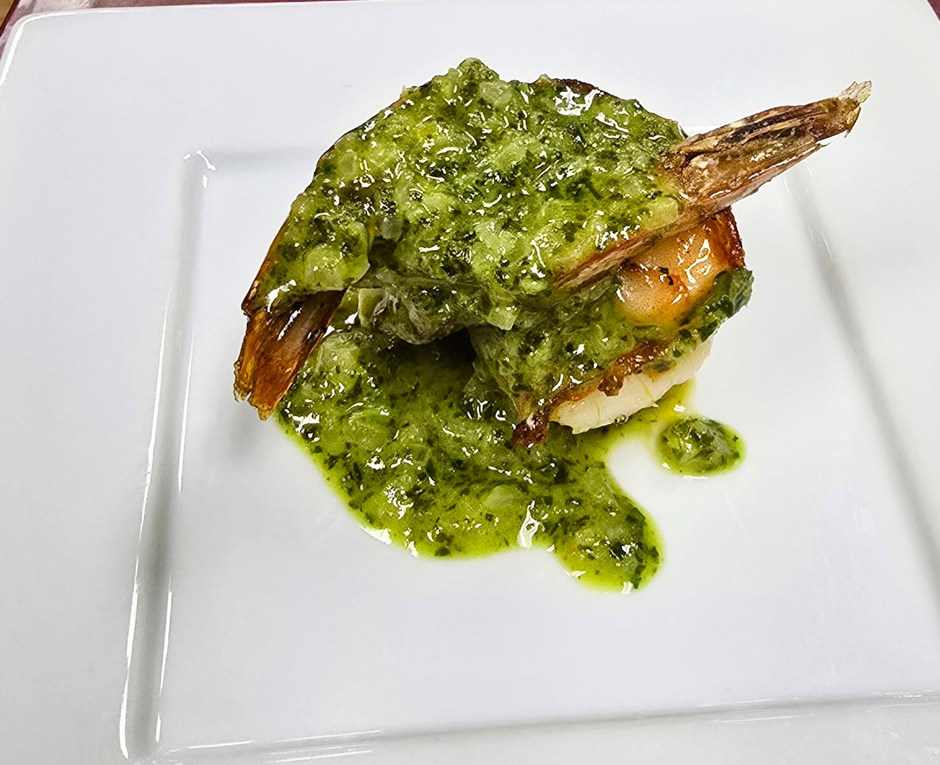 Grilled shrimp topped with green sauce on a white plate.
