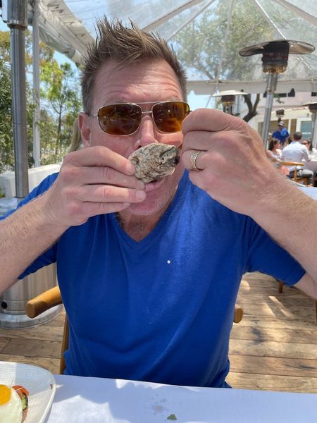 A man wearing sunglasses is eating an oyster