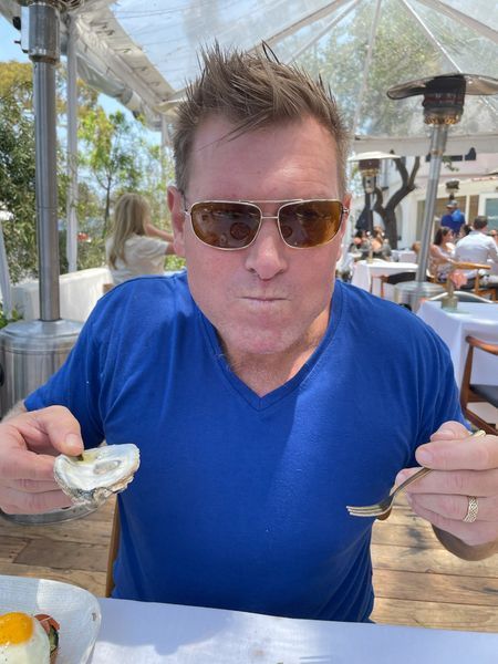 A man wearing sunglasses is eating an oyster with a fork