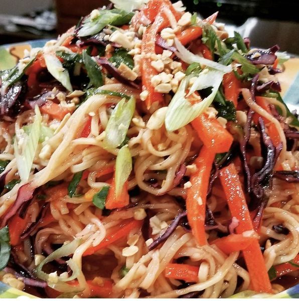 A plate of noodles and vegetables with sesame seeds on top
