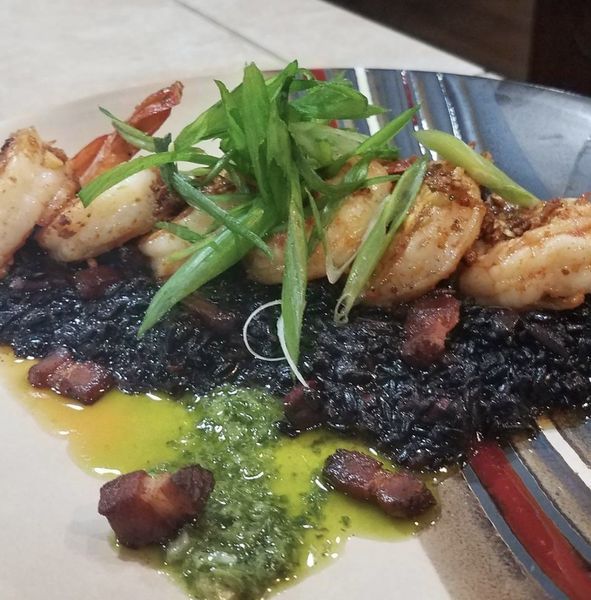 A plate of food with shrimp on top of black rice
