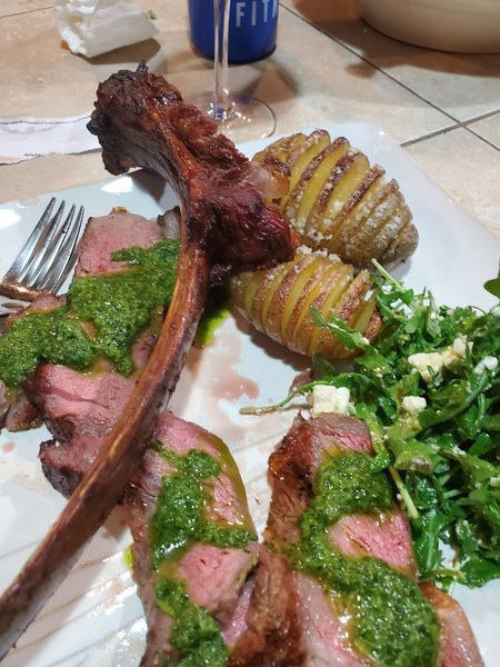 A white plate topped with meat and potatoes with a glass of wine in the background