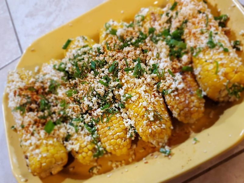 Corn on the cob with cheese and cilantro on a yellow plate.