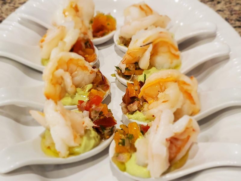 A white plate topped with spoons filled with shrimp and guacamole.