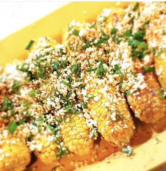 Corn on the cob with cheese and green onions on a yellow plate