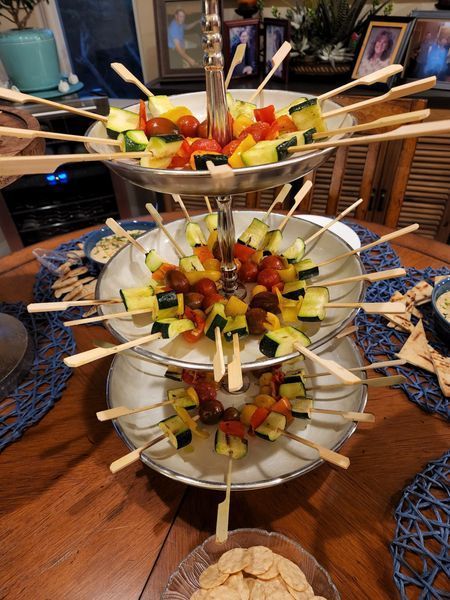 A three tiered tray filled with vegetables on skewers on a table.