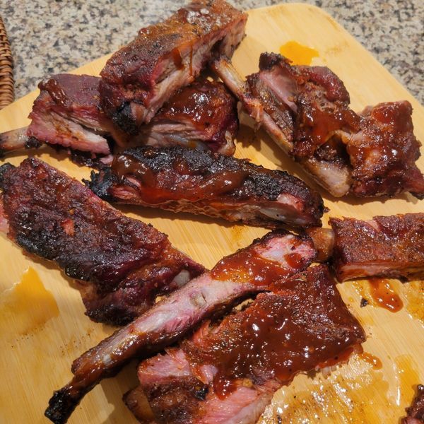 A wooden cutting board topped with ribs and sauce
