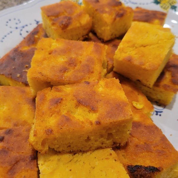 A close up of a plate of cornbread squares on a table.
