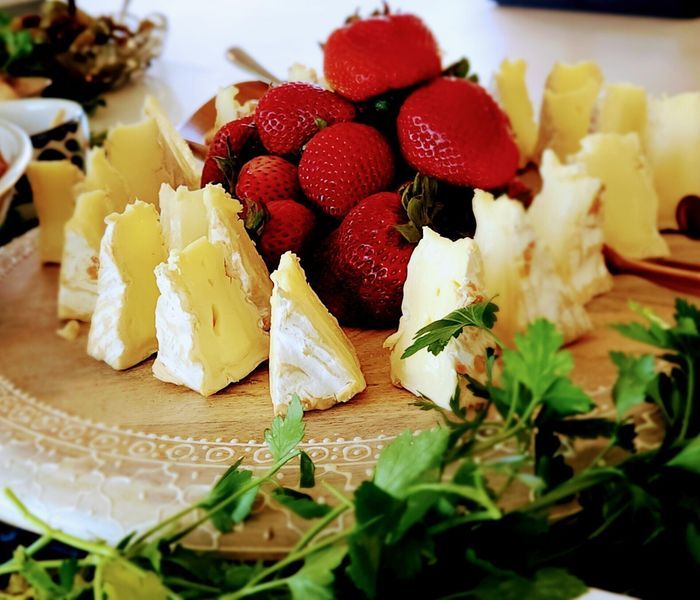 A wooden cutting board topped with cheese and strawberries.