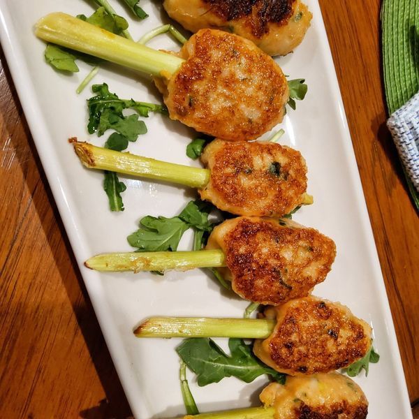 A white plate topped with meatballs and greens on sticks