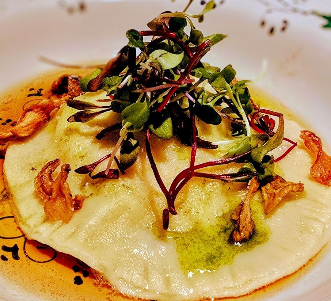 Ravioli dish with herbs and mushrooms, in a shallow bowl, with a light sauce.