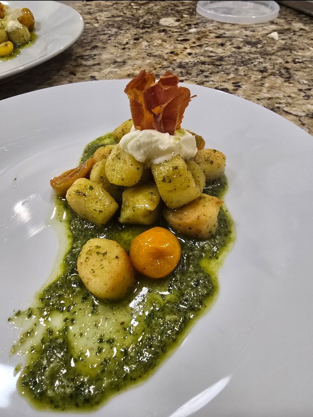 Gnocchi dish with pesto, tomato, and prosciutto on a white plate, with a marble countertop in the background.