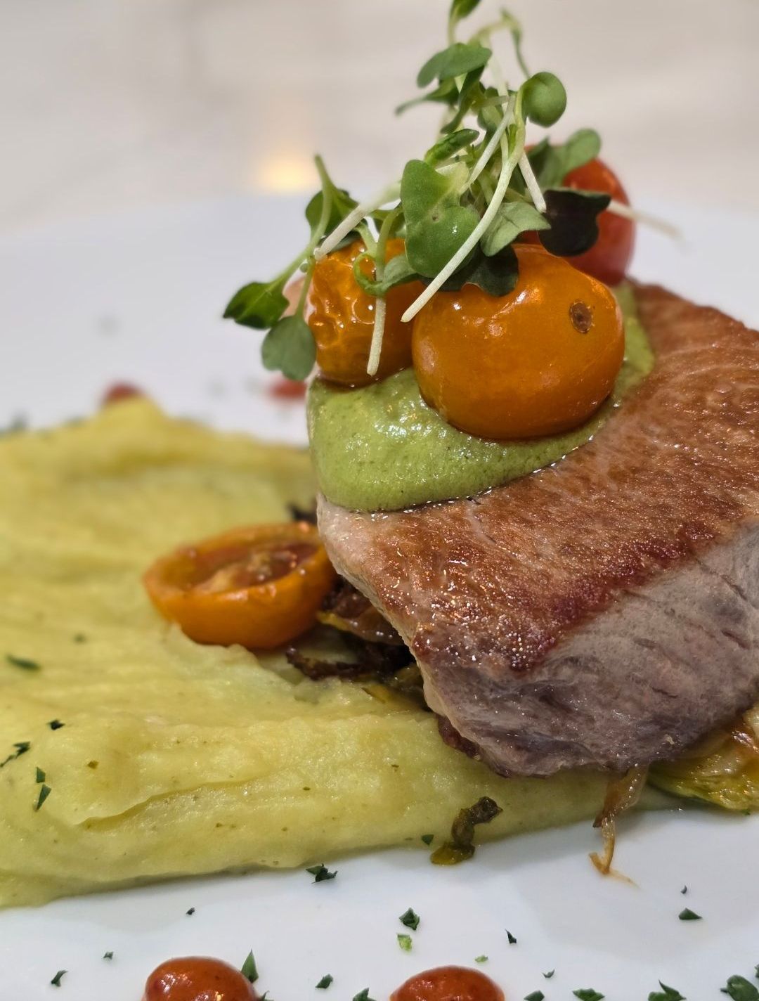 Seared tuna steak with mashed potatoes, cherry tomatoes, and microgreens on white plate.