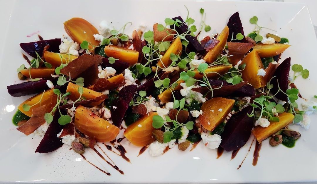 Beet salad with golden and purple beets, goat cheese, microgreens, and balsamic glaze on a white plate.