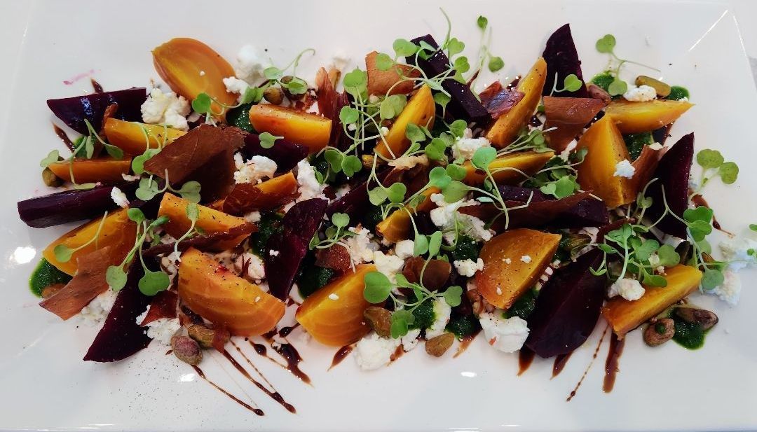 Beet salad with orange and purple beets, feta, sprouts, and balsamic glaze on a white plate.