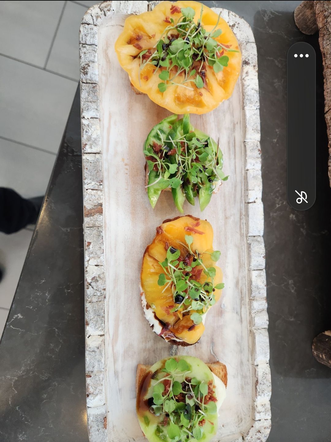 Four bruschetta topped with various ingredients in a rustic wooden tray.