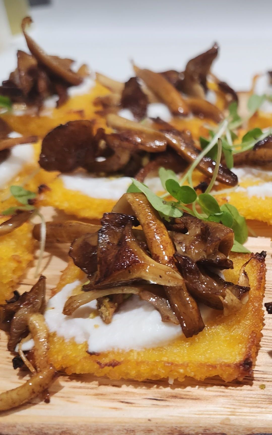 Polenta squares topped with ricotta cheese and sautéed mushrooms, garnished with microgreens.