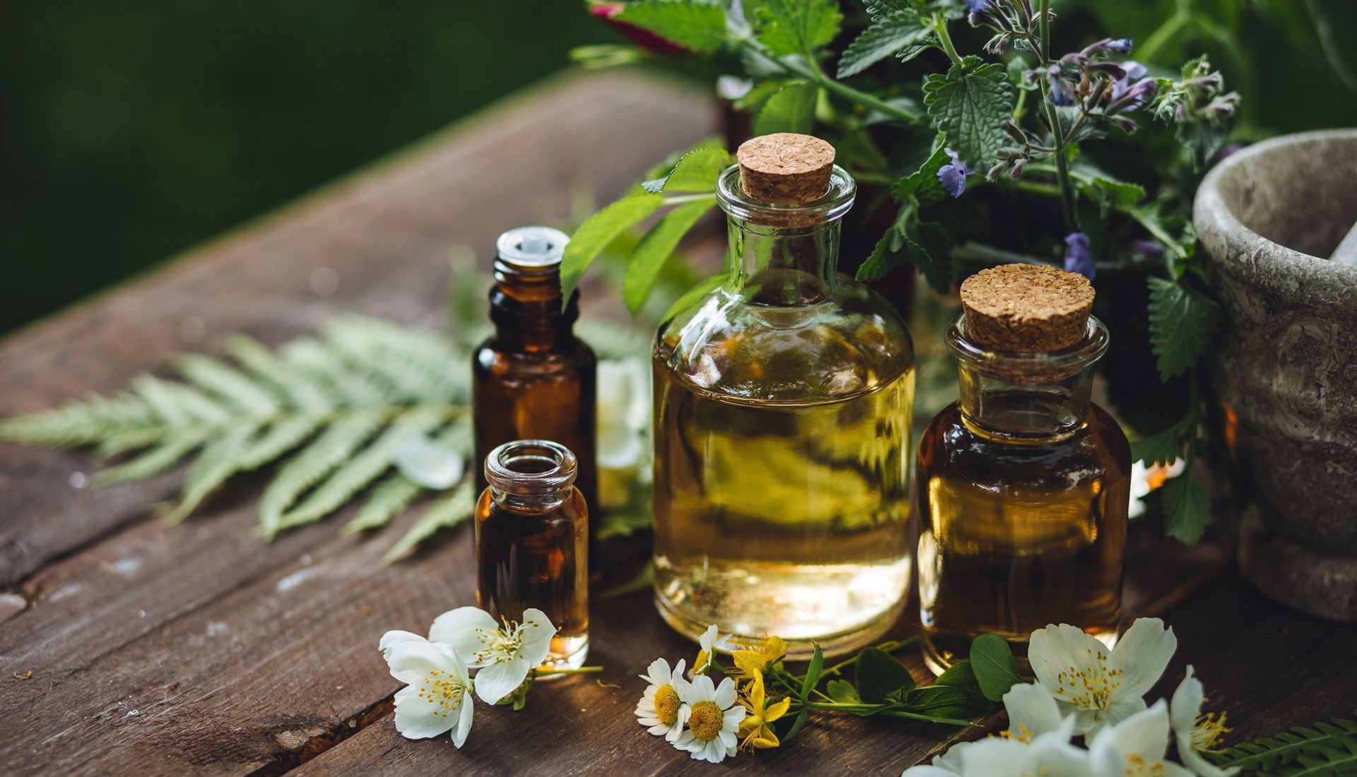 Bottles of essential oils with corks, flowers, and greenery on a wooden surface.