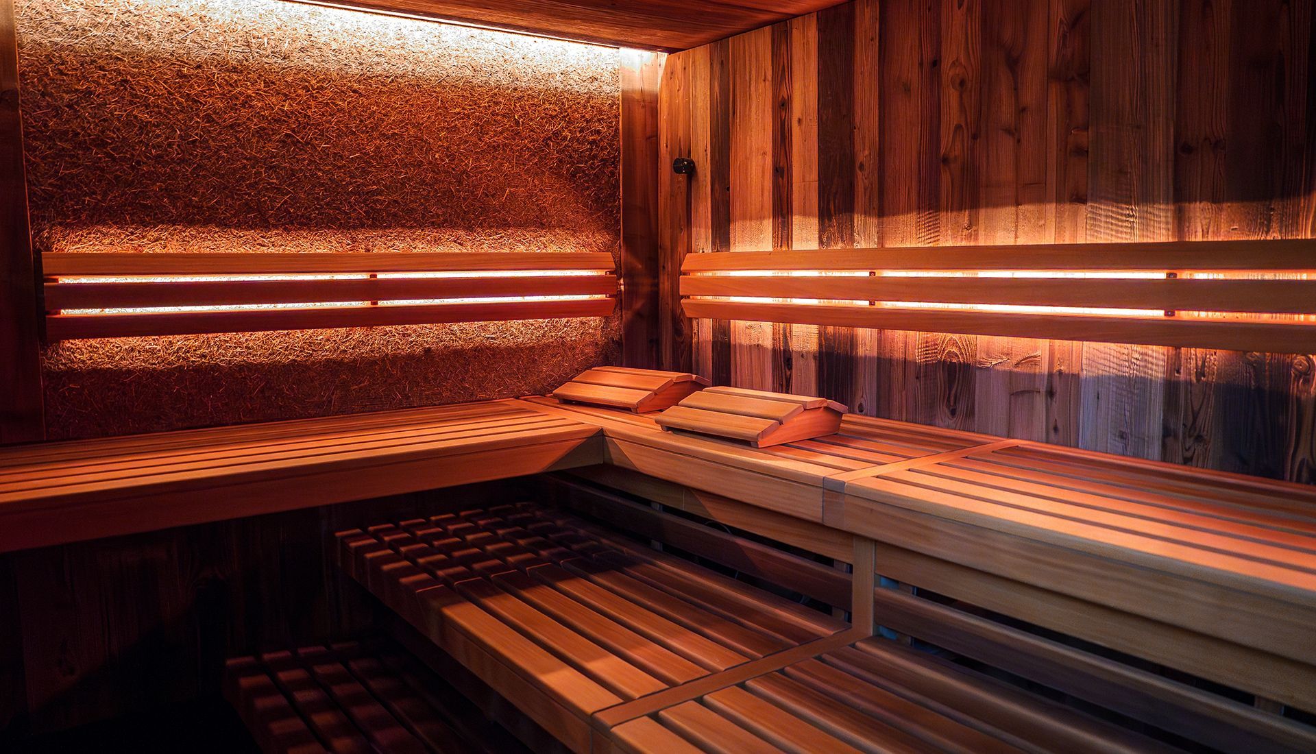 Wooden sauna interior with benches, soft lighting, and pillows.