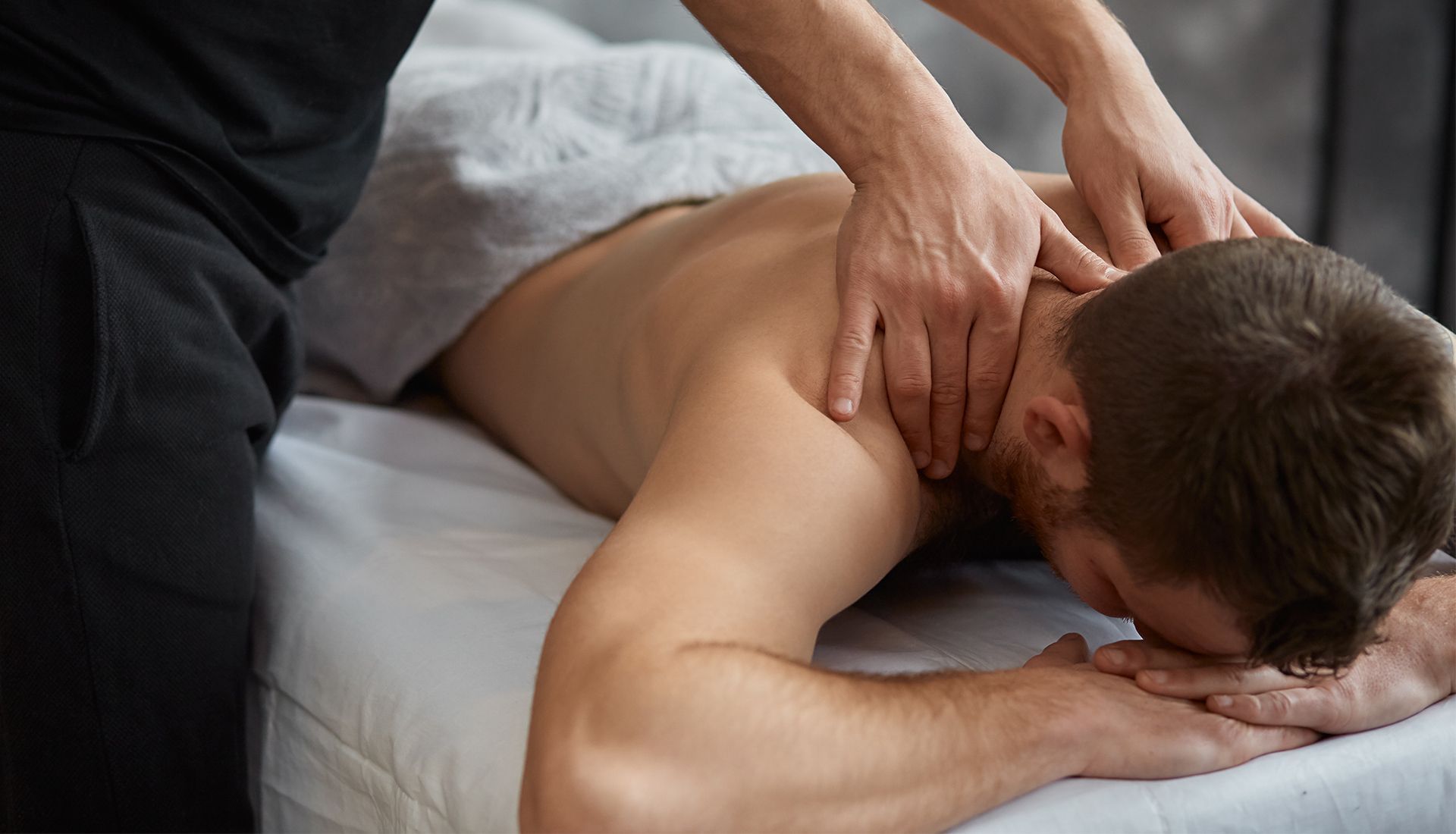 Person receiving a back and neck massage, face down on a massage table. Hands of therapist on neck.