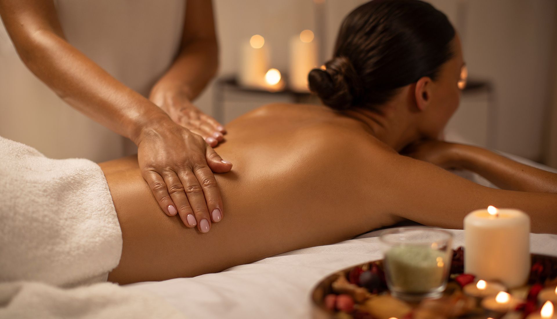 Person receiving a back massage in a dimly lit room with candles and a tray.
