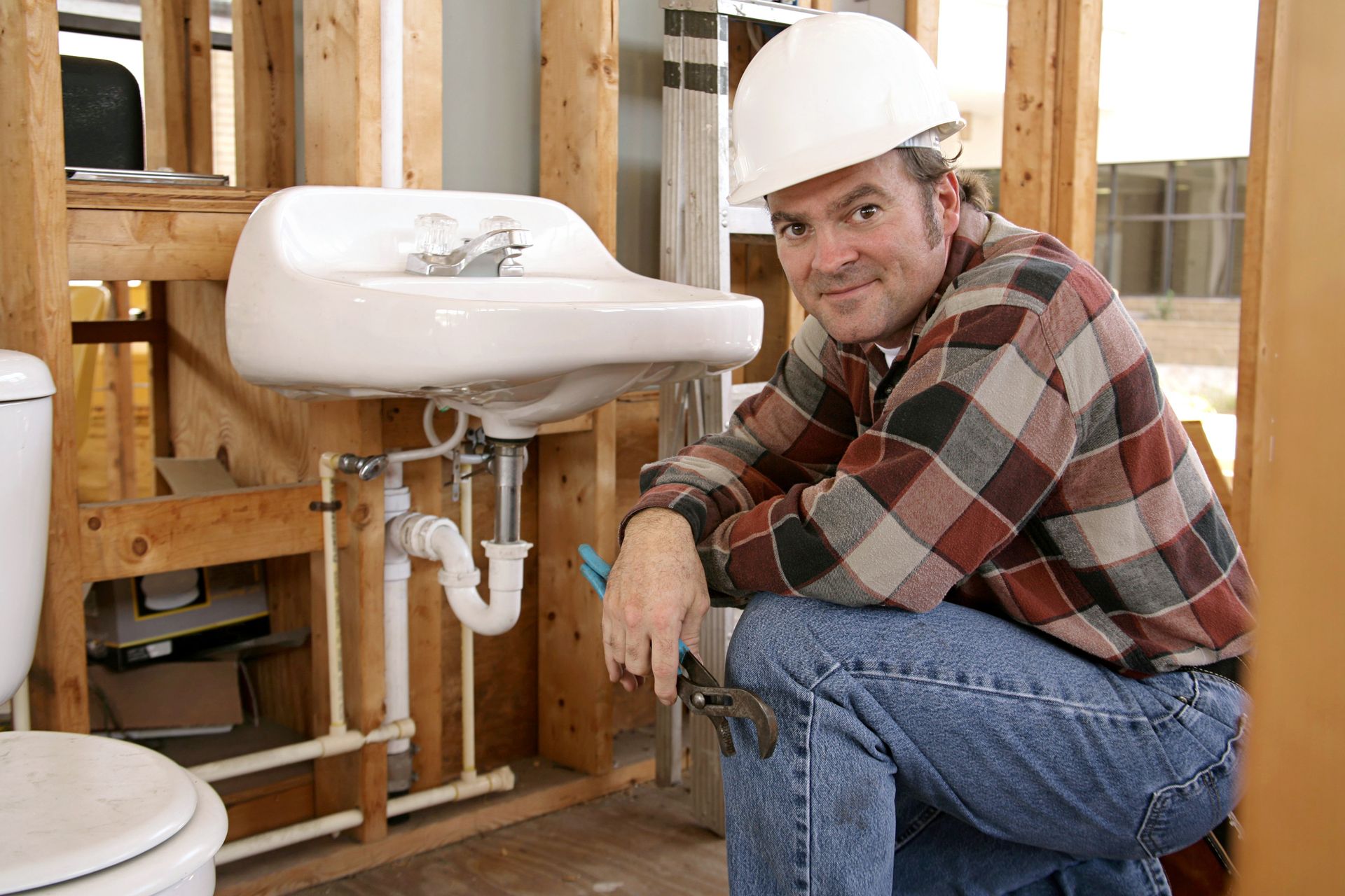 A plumber is looking into the camera, kneeling next to an installed bathroom sink.