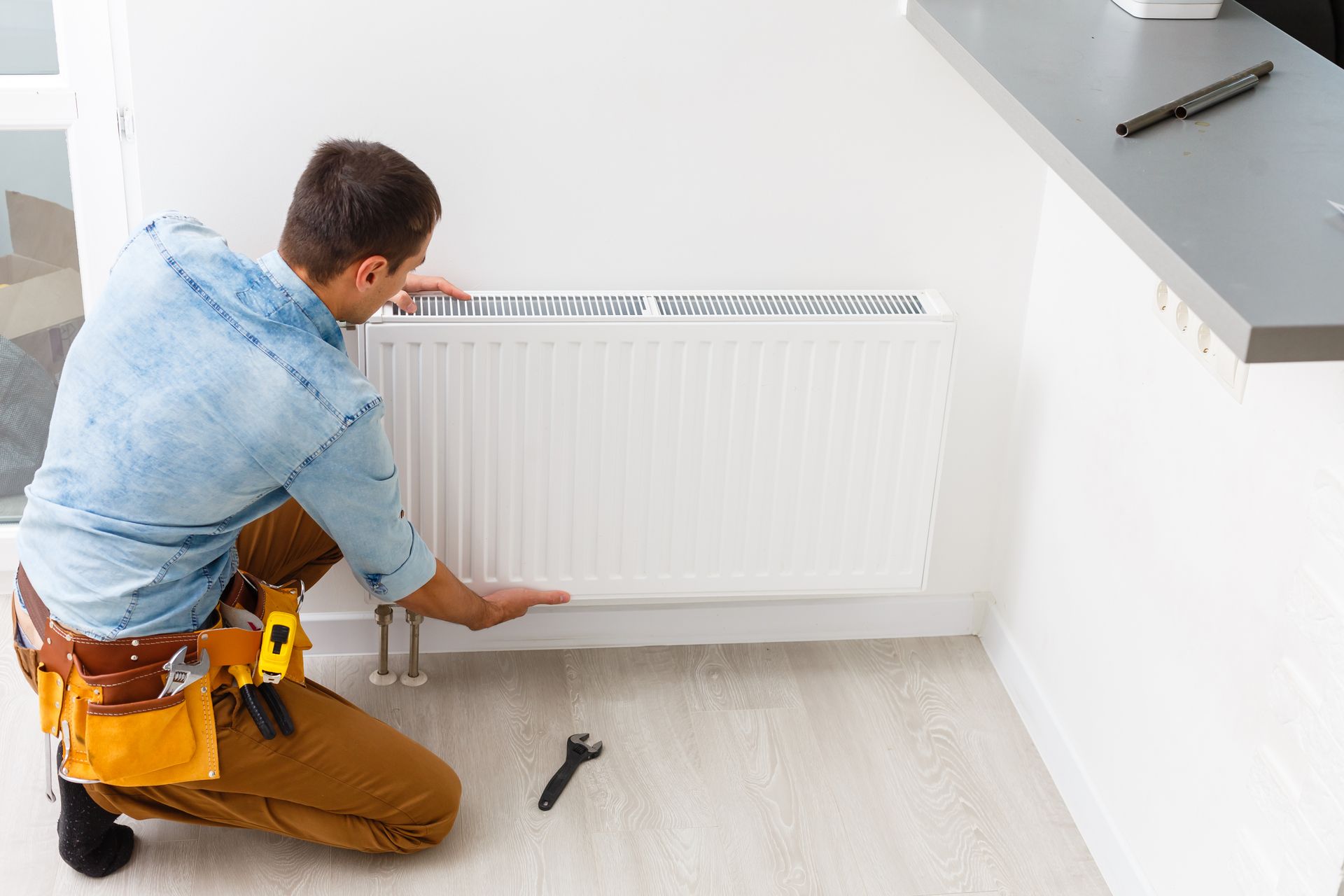 Worker adjusting a wall-mounted radiator during routine heating maintenance.