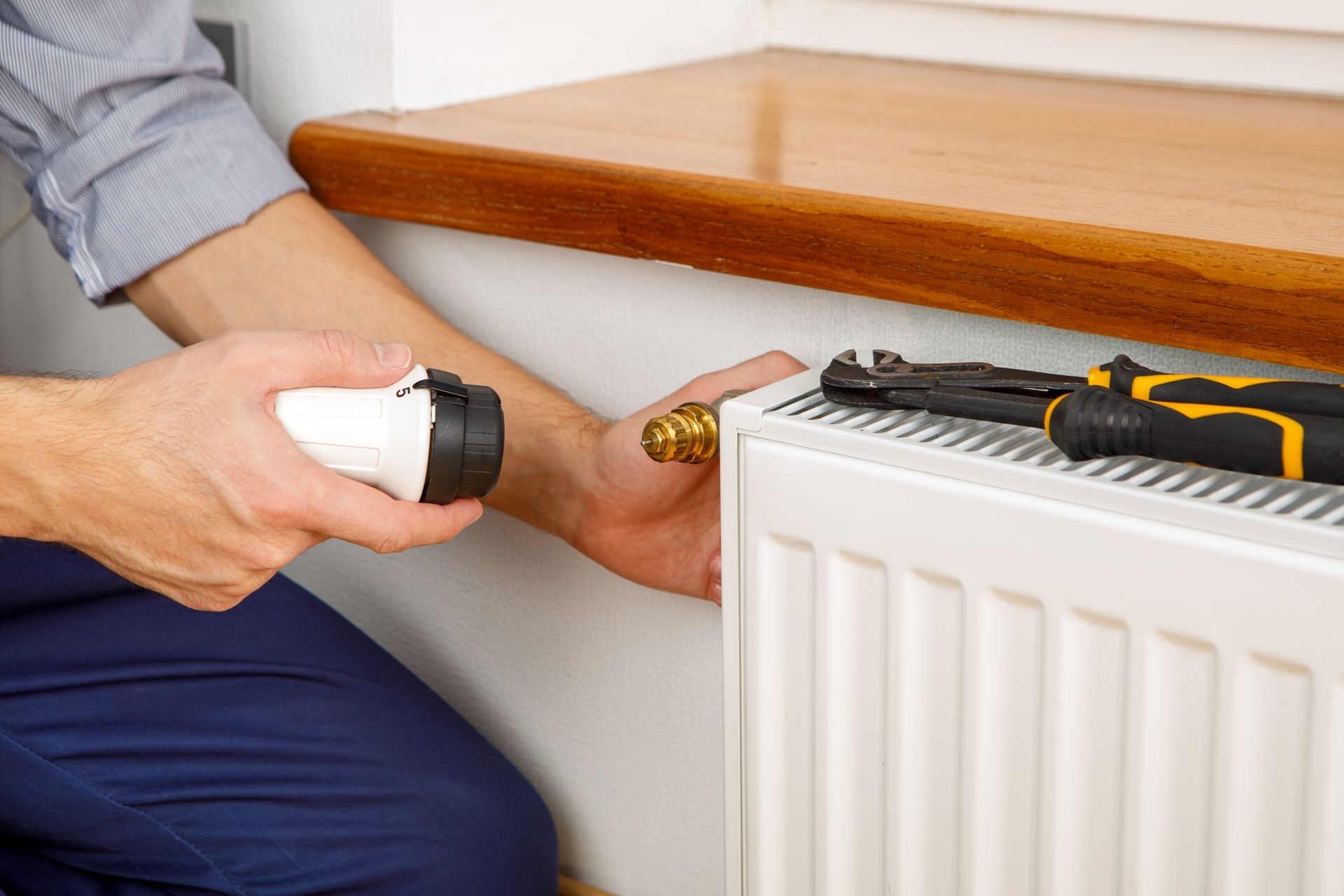 Worker installing a new thermostat valve on a wall-mounted radiator.