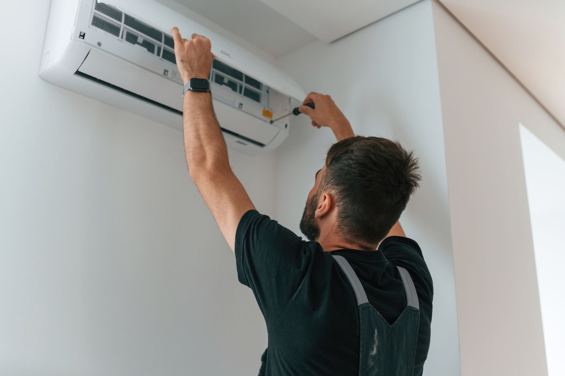 A technician is servicing an air conditioner with a screwdriver.