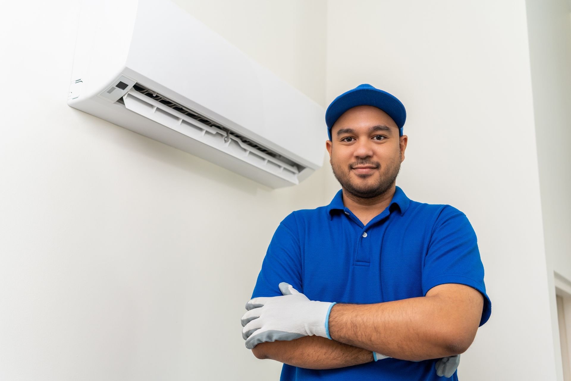 An air conditioner contractor in front of a cleaned AC unit in uniform wearing rubber gloves.
