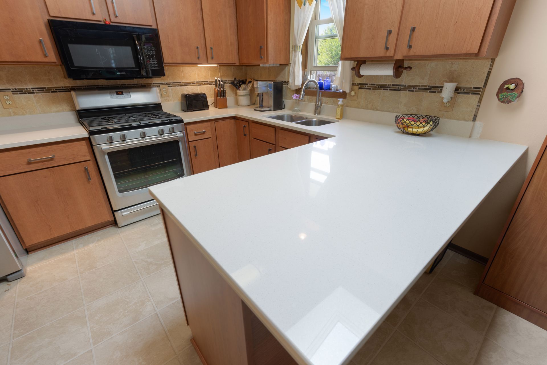 Kitchen with light countertops, wooden cabinets, stainless steel appliances, and a window.