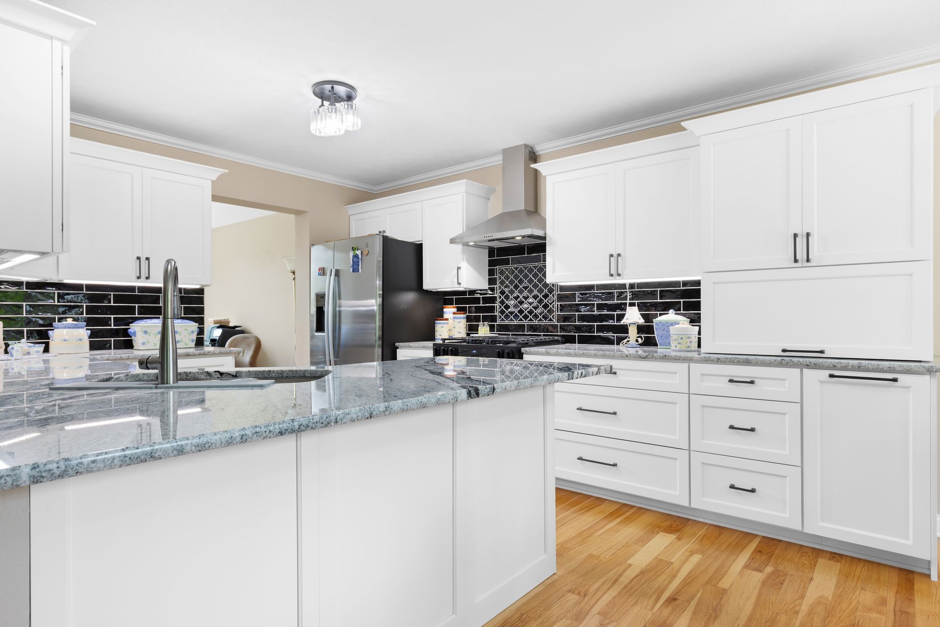 White kitchen with granite countertops, stainless steel appliances, and wood floors.