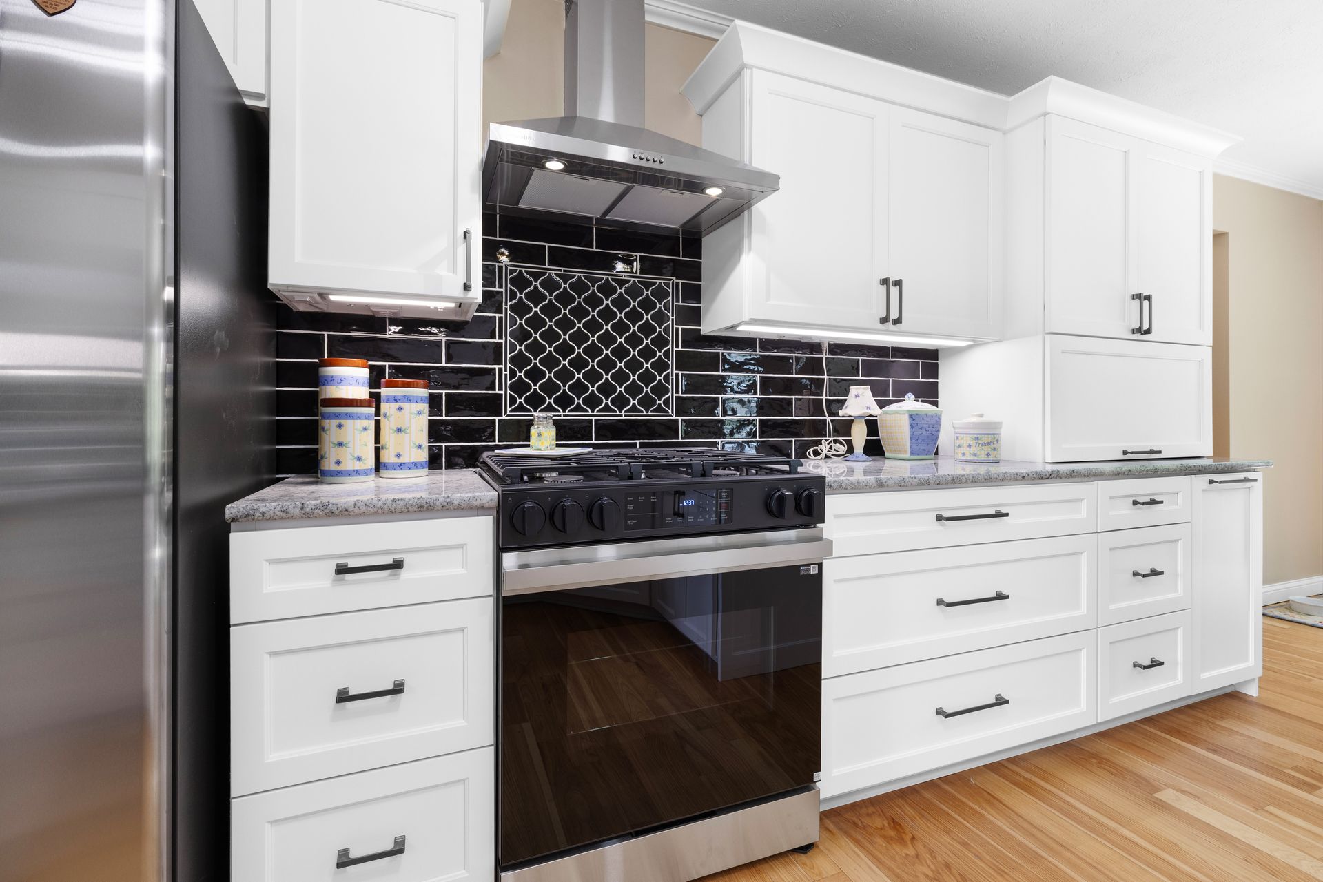 White kitchen cabinets with black backsplash and stainless steel appliances.