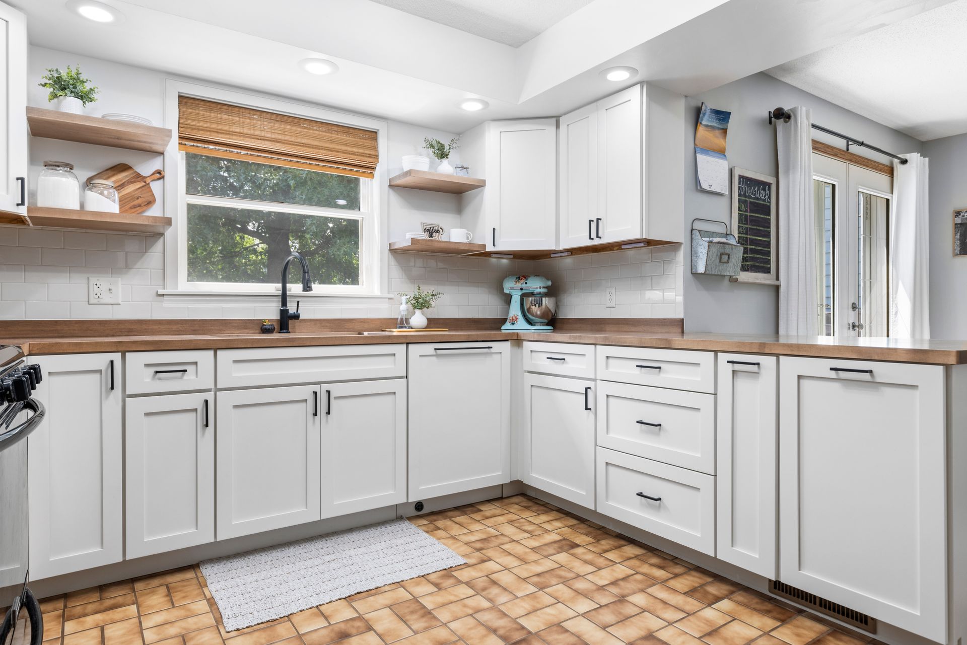 White kitchen with wood countertops and floors, window with woven shade.