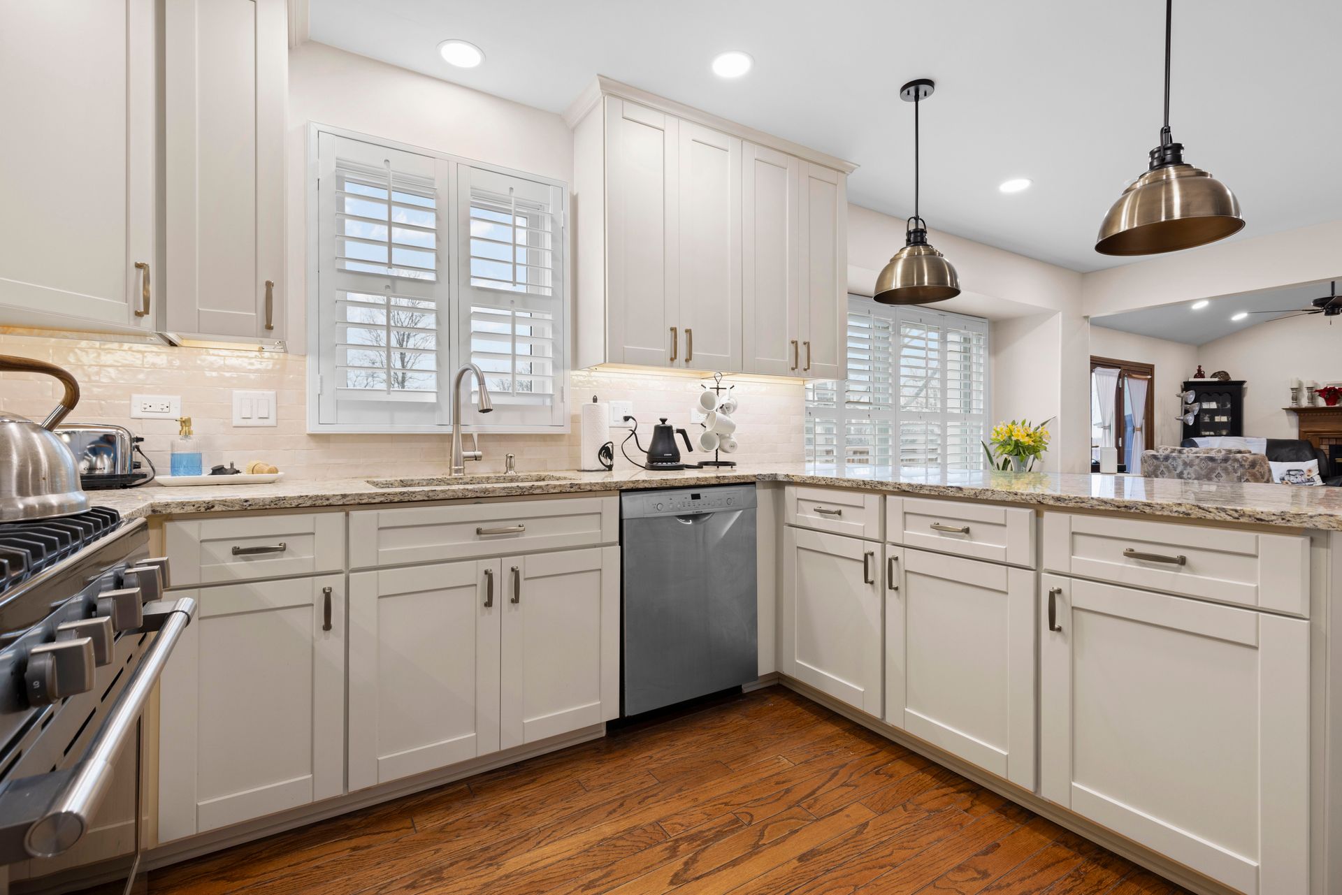 Cream-colored kitchen with granite countertops, stainless steel appliances, wooden floor, and pendant lights.