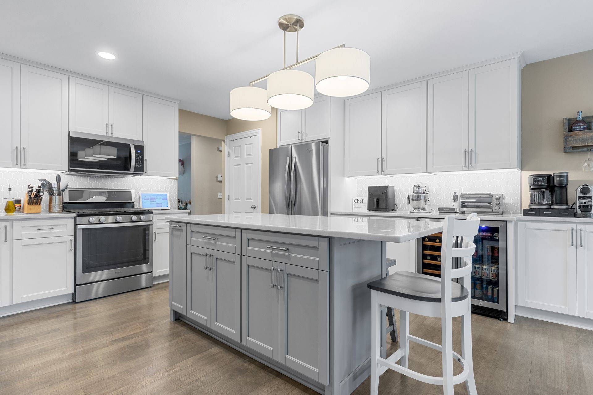 Modern kitchen with white cabinets, gray island, stainless steel appliances, and wooden floor.