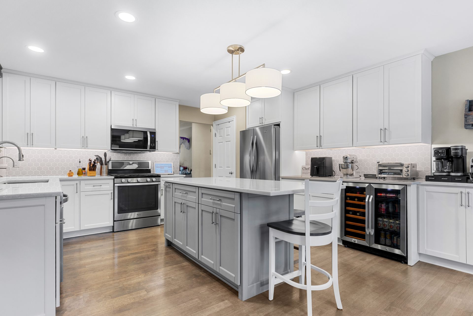 Bright kitchen with white cabinets, gray island, stainless steel appliances, and wood floors.