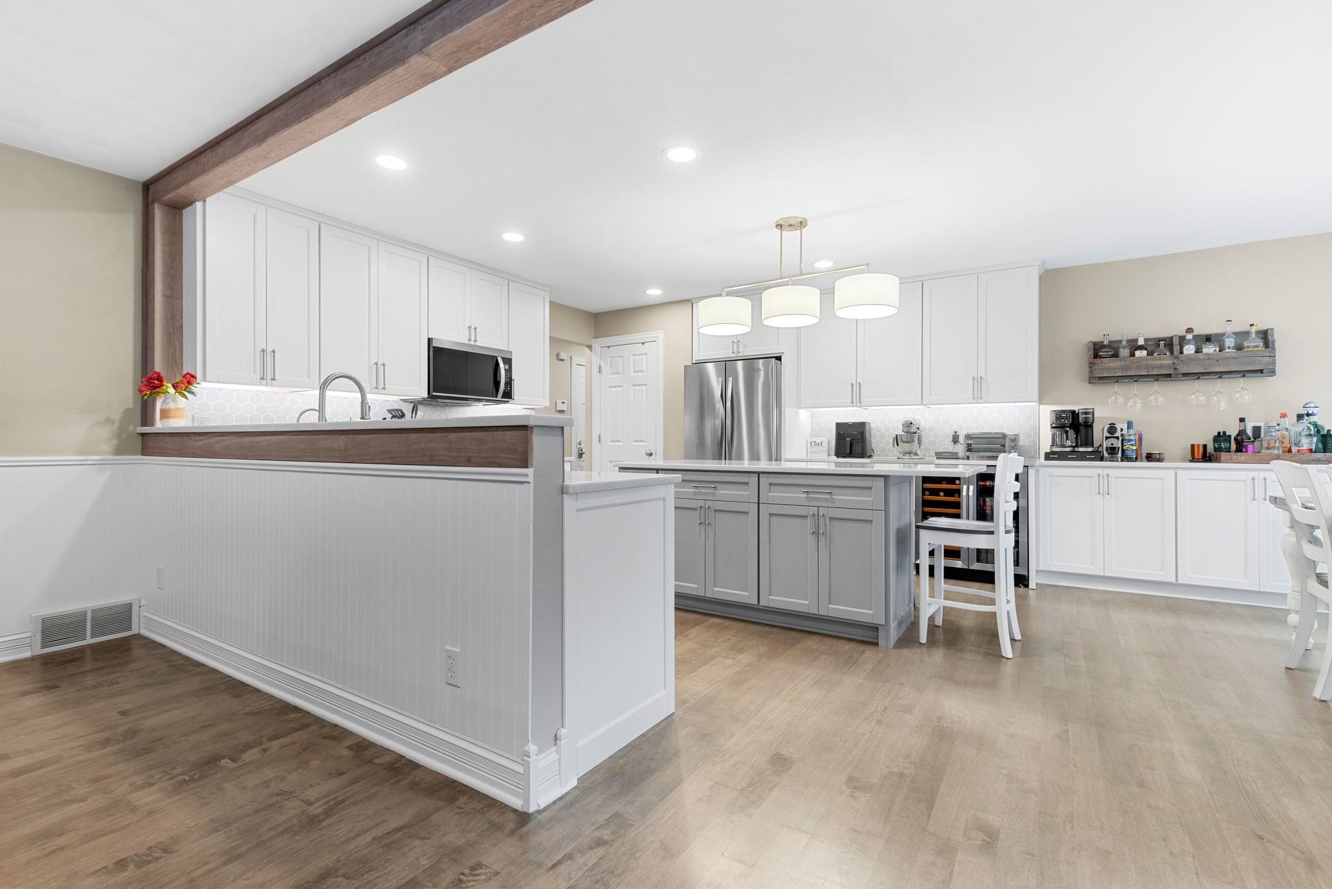 Modern white kitchen with gray island, light wood floors, and a wooden beam.